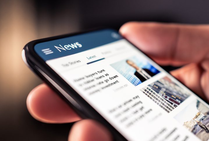 Person holding a smartphone displaying a news website.