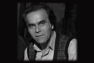 Black and white portrait of a man with intense eyes and a slight smile.