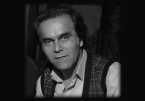 Black and white portrait of a man with intense eyes and a slight smile.